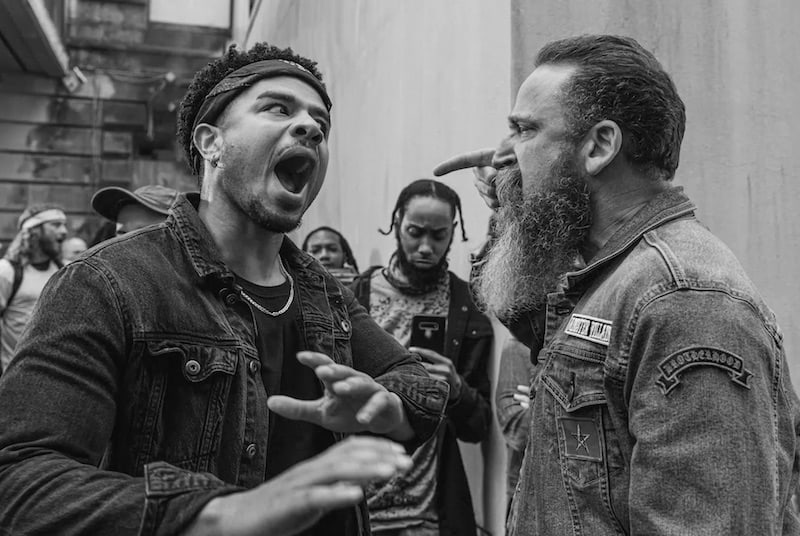 This black and white image shows two bearded men in casual clothing are shown an animated conversation.